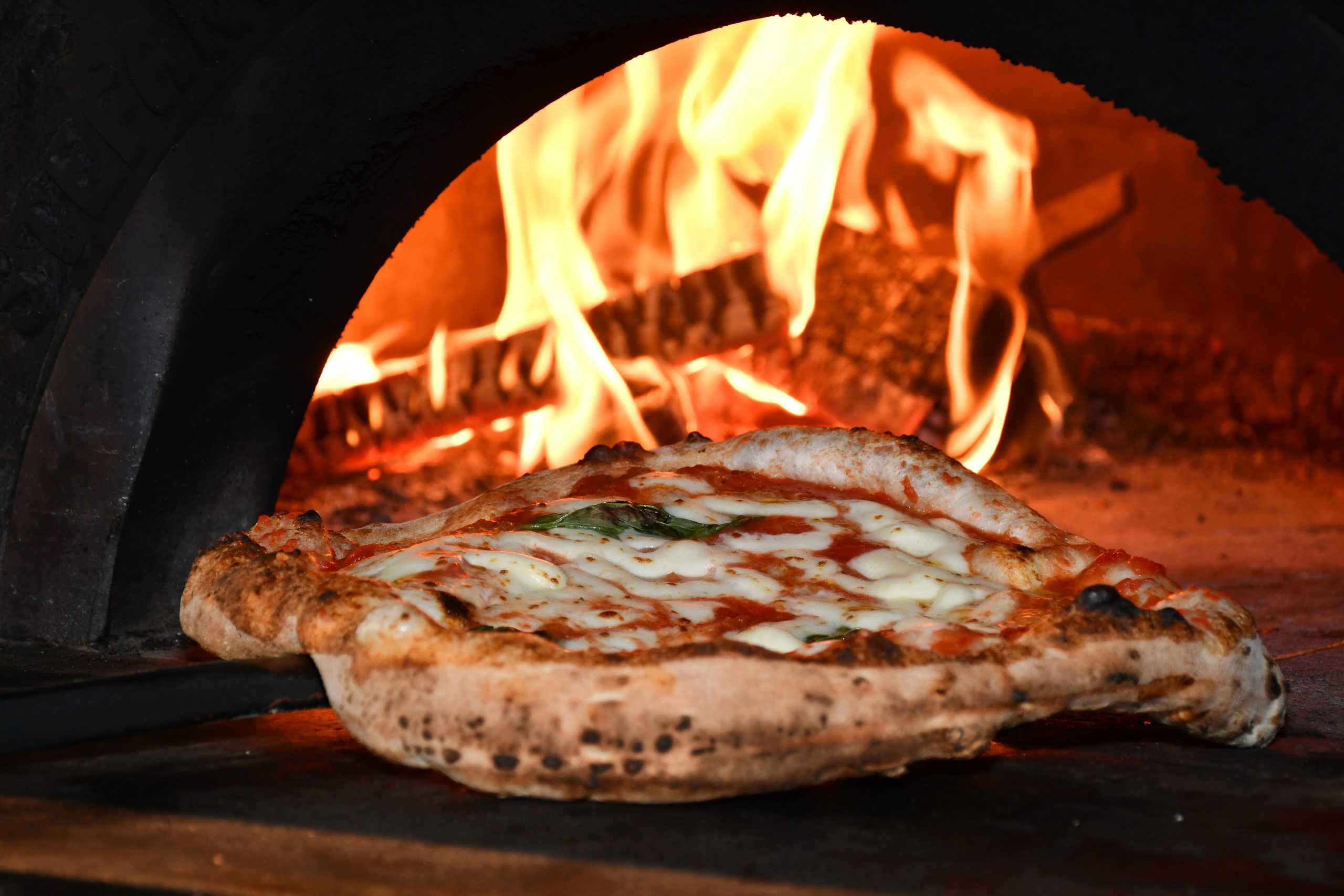 A pizza being taken out of a wood-fired oven.